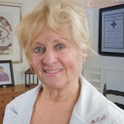 Woman with gray hair, wearing a light-colored jacket and black shirt